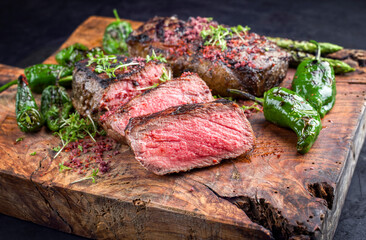 Traditionell gegrilltes dry aged Wagyu Roastbeef Steak mit grünen Spargel und Chili angeboten als close-up auf einem alten rustikalen Holz Board