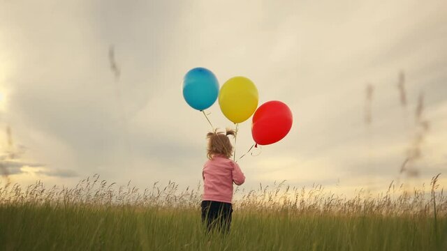 A little lovely girl, a happy child running on the green grass with colorful balloons in her hands. The concept of freedom, a child's dream, a happy family.