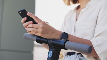 Woman is using smartphone after ride on electric kick scooter
