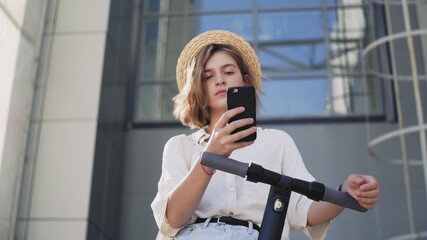 Woman is using smartphone after ride on electric kick scooter © stanis88