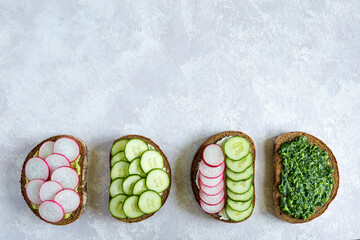Obraz na płótnie Canvas Homemade sandwiches with radish, pesto, cucumber and cheese on the gray background. Slices of vegetables on bread. Healthy snack. Flat lay, top view, place for text.