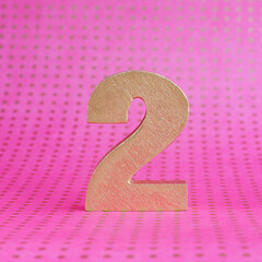 Golden volumetric number 2 on a bright pink polka dot background. copy space..