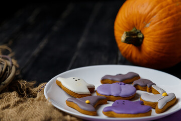 Obraz na płótnie Canvas Pumpkin and Halloween cookies on white plate, sackcloth on black wooden background. Hallooween trick or treat concept. Copy space.