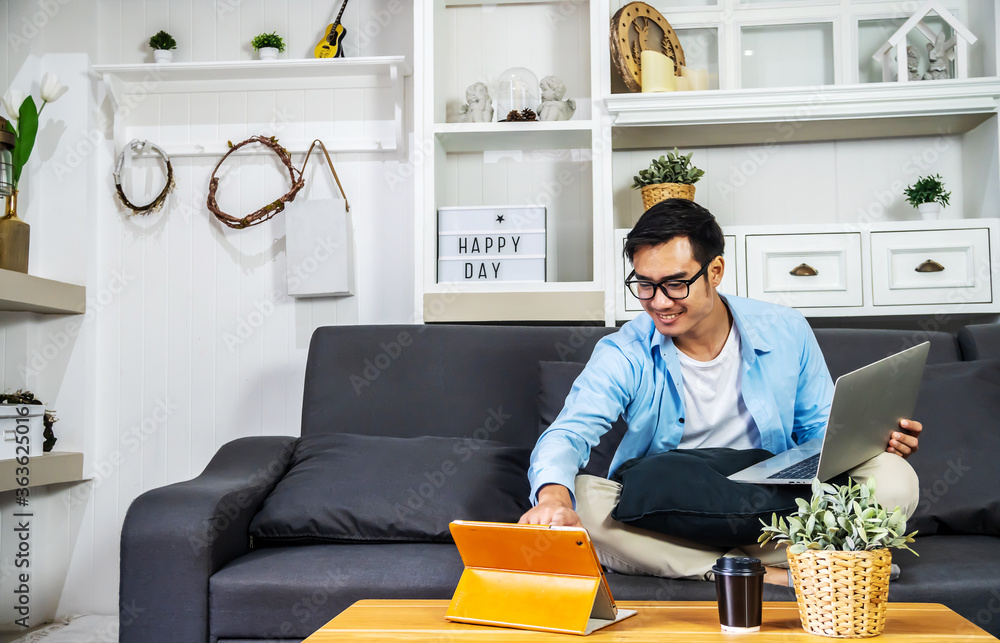 Wall mural smart asian businessman in casual clothing sitting on a sofa in the house is working on computer lap