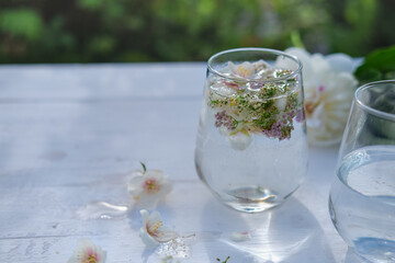 garden wedding drinks. transparent non alcoholic drink with flower decoration. outdoors wedding. white flowers in a tonic water. wooden table with glasses on it.