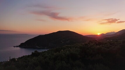 sunset over the sea with silhouette of a hill and olive trees 