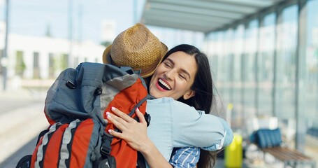 Beautiful Caucasian young brunette woman smiling and meeting boyfriend or husband outdoor at bus stop. Coming back home from trip. Couple in love meet Rear of guy traveller hugging girlfriend Close up