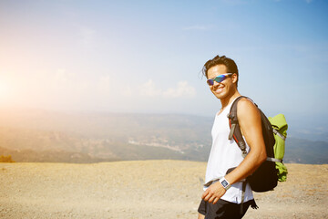 Young smiling man wanderer with sporty backpack posing for photo on the memory while standing on a...