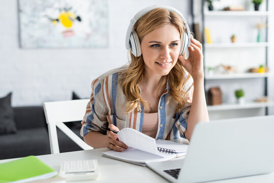 Selective focus of attractive woman in headphones looking at laptop while studying online