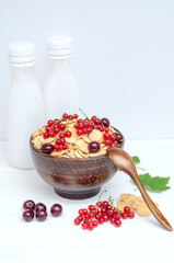 Fresh cornflakes with currants and cherries in a round bowl on a wooden background.