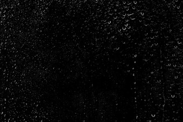 Drops of water flow down the surface of the clear glass on a black background. Texture for creativity.