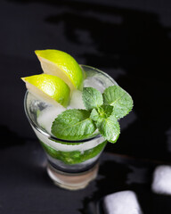 Mojito cocktail with lime, mint green and ice on dark wooden table, selective focus