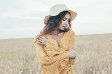 Portrait of a girl of model appearance on the field in a hat and dress
