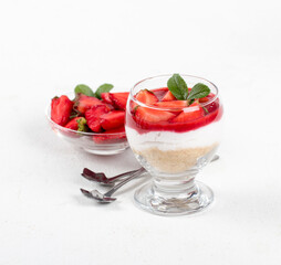 Dessert cheesecake with cookies, cream cheese, strawberry sauce and strawberry slices in a glass on a white background