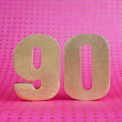 Golden volumetric number 90 on a bright pink polka dot background. copy space..