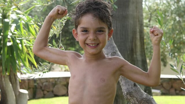 Bambino biondo sorride gioca e mostra scherzosamente i muscoli nel giardino di casa