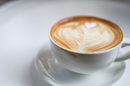 Closeup Of White Cup Of Hot Coffee Latte With Milk Foam Heart Shape Art With Dirty Lip Marks On White Table.