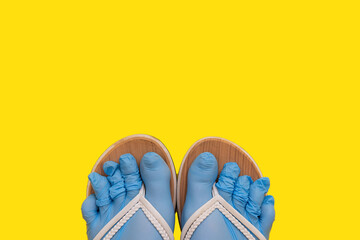 Legs of a girl dressed in rubber blue medical sterile gloves, shod in white flip flops on an orange yellow plain background. A joke of a safe rest on the sea in the sand, protection against a virus