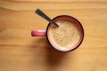 Pink cup with freshly made coffee resting on a wooden table with a metal spoon