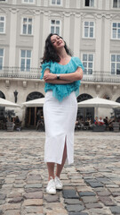 Fototapeta premium Young Caucasian woman with turquoise blouse curly hair standing im the street urban old city bacgkround. Portrait close up of young beautiful brunette woman.