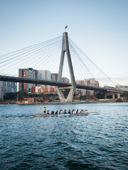 Rowing team on river in front of bridge at dusk
