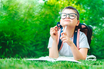 Surprised school child in glasses pointing finger up showing new idea. Happy kid boy writing homework on green background. Online education e-learning concept. Back to school