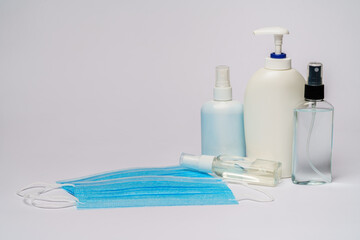 bottle of lotion, sanitizer or liquid soap and protective mask over light grey background