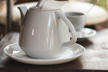 white teapot for brewing tea with a cup on a wooden dark surface, table