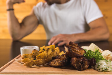 delicious kebabs, pita bread with fried potatoes lie on a wooden tray on the table in a pub or tavern. in the background a man shows biceps on his arm. Close up view. For the menu