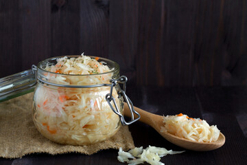 homemade sauerkraut with carrots with herbs in glass jar on a black background. Pickled cabbage in a spoon with sackcloth on the wooden table. The concept of canned food. copy space. vegetarian food.