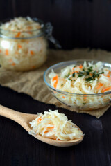 homemade sauerkraut with carrots with herbs in glass plate on a black background.Pickled cabbage in spoon with sackcloth on the wooden table.copy space.The concept of canned food.vegetarian food.