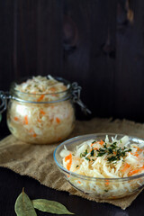 homemade sauerkraut with carrots with herbs in glass plate on a black background. Pickled cabbage in a jar with sackcloth on the wooden table. The concept of canned food. copy space. vegetarian food.