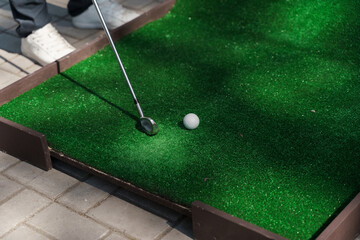 Playing in mini-golf on the green grass using niblick. Player hits white ball. Golf sport game. Advert for golf club