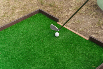 Playing in mini-golf on the green grass using niblick. Player hits white ball. Golf sport game. Advert for golf club