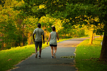 Image of an African American man and a caucasian woman walking on a hiking trail outdoors. The couple wears marching vests, shirts, shorts and sneakers. They wear face masks for COVID 19 pandemics