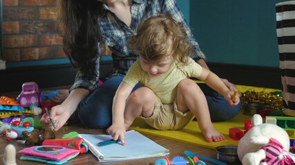 Mother and daughter draws in a notebook on the floor