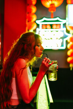 side view of a woman long hair drinking from a straw a glass of soda or alcohol in a night club bar