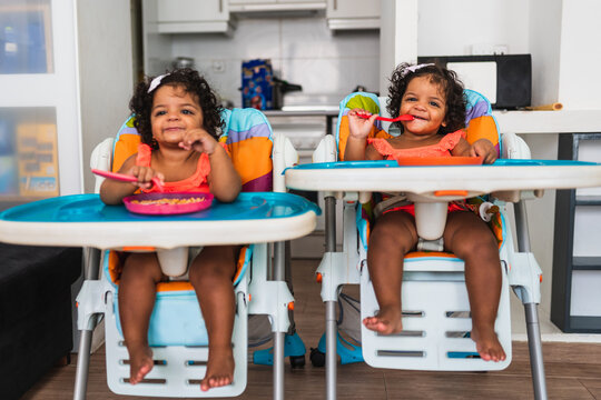 Identical Adorable Twin Girl On Their Baby Feeding Chair.