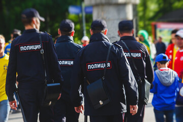 Russian police squad formation back view with "Police" emblem on uniform maintain public order after football game with football fans crowd in the background