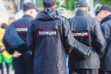Russian police squad formation back view with "Police" emblem on uniform maintain public order after football game with football fans crowd in the background