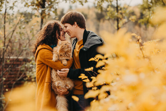 Young couple with a red cat on a background of an autumn park.