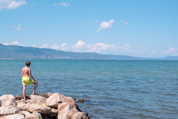 Fototapeta na wymiar Teenage boy is standing on a rocks on a seashore