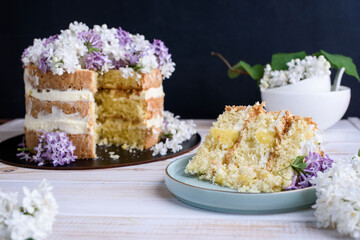 Biscuit cake with cream, impregnated with coconut and pineapple, decorated with lilac flowers.