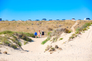 Fototapeta na wymiar People in swimsuits leaving the beach for a parking located on a sandy hill.