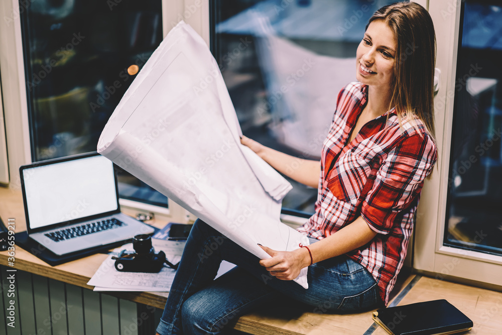 Poster smiling woman holding papers with drawings satisfied with completing blueprint before deadline sitti