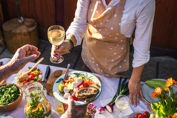 Enjoy white wine and vegetable salad at garden party. Woman is serving food and drink to another person at celebration event outdoors