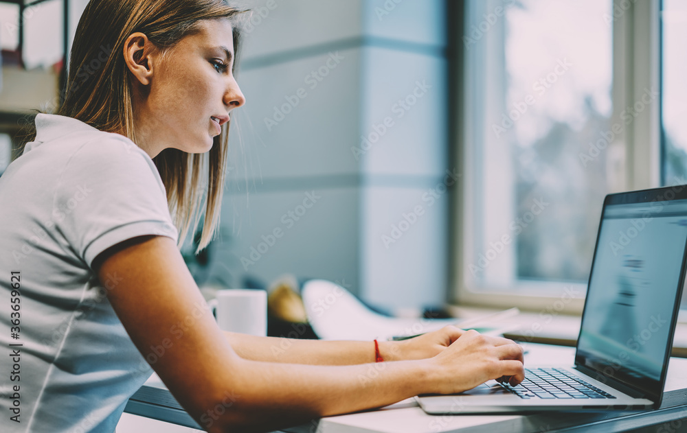 Poster pensive young woman typing text for course work on modern netbook and searching information on websi
