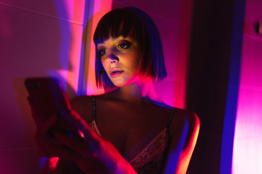 Beautiful girl using her smartphone on the neon light.