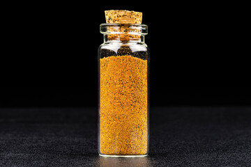 Macro shot of nutmeg spice in a small glass bottle closed with a cork, isolated on a black background.