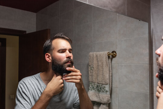 Focused guy checking beard near mirror
